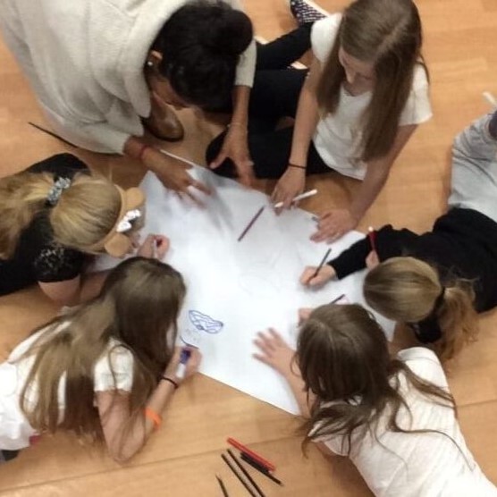 Children lying in a circle around a large sheet of paper, each of them is drawing on it